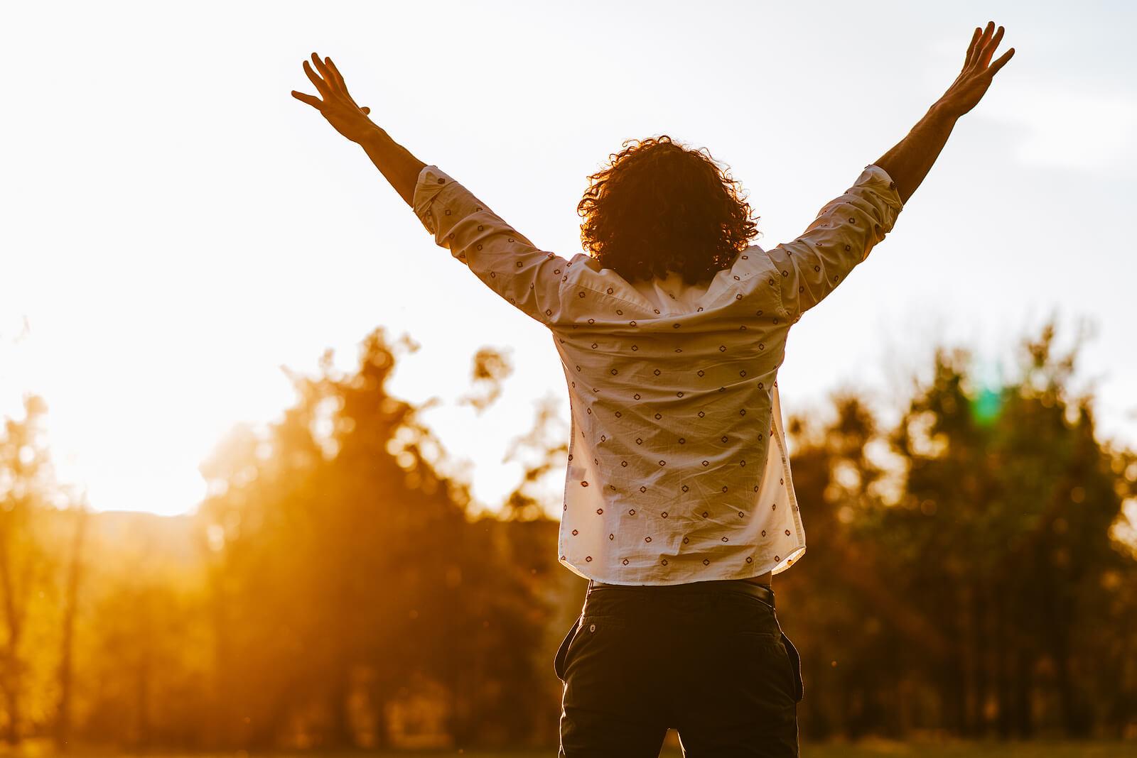 Image of a positive man standing outside as the sun sets with his arms raised in the air. Find the extra care you deserve with the help of an adult intensive outpatient program in Houston, TX.