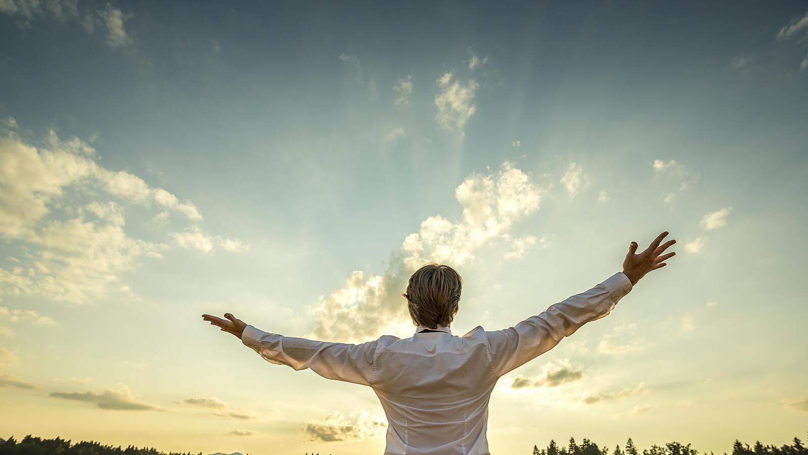 Image of a positive man standing outside during sunrise with his arms in the air. If your hopelessness is feeling unmanageable begin to cope and start thriving with Adult IOP in Houston, TX.