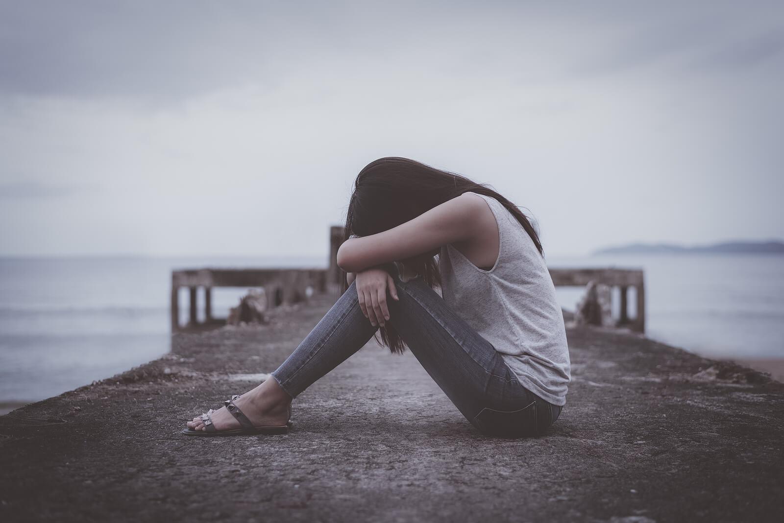 Image of a depressed young woman sitting on a pier with a dark cloudy sky. Begin to cope and heal from your depression with the help of an adult intensive outpatient program in Houston, TX.
