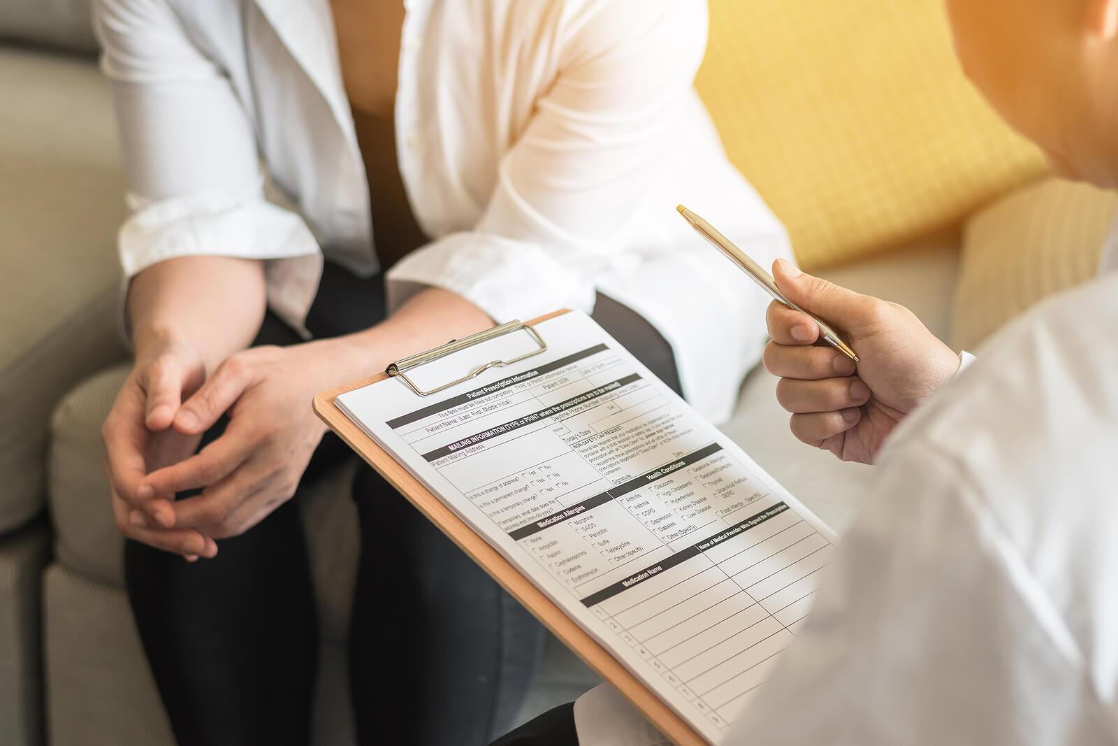 Image of a woman holding a clipboard speaking to a woman sitting on a couch. If you're unable to effectively manage your emotions, find support with adult iop in Houston, TX.