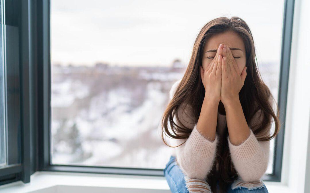 Image of an anxious woman sitting in a window sill covering her face with her hands. If you struggle with anxiety, discover how learning DBT at an adult intensive outpatient program in Houston, TX can help you.