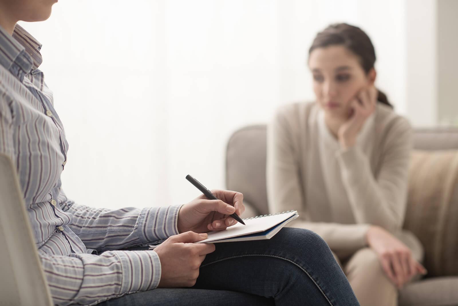 Image of an upset young woman sitting on a couch across from a woman holding a notepad and pen. Overcome the BPD symptoms you struggle with by finding support with an adult intensive outpatient program in Houston, TX.