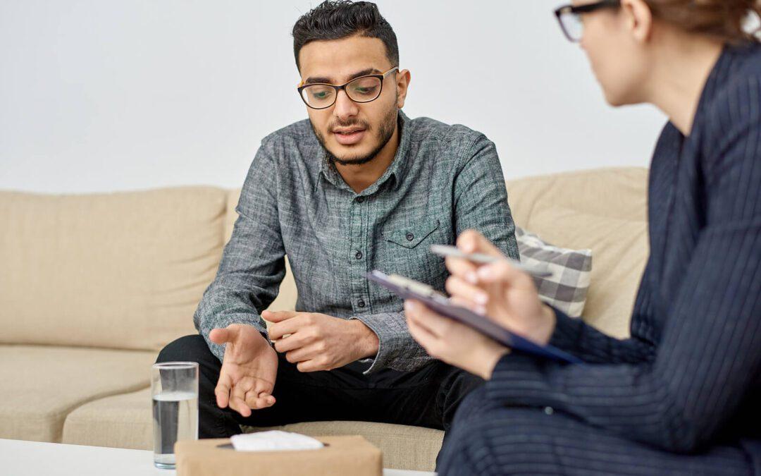 Image of a young man sitting on a couch speaking to a woman holding a clipboard. If you struggle with BPD, discover how and adult intensive outpatient program in Houston, TX can help you manage your symptoms.