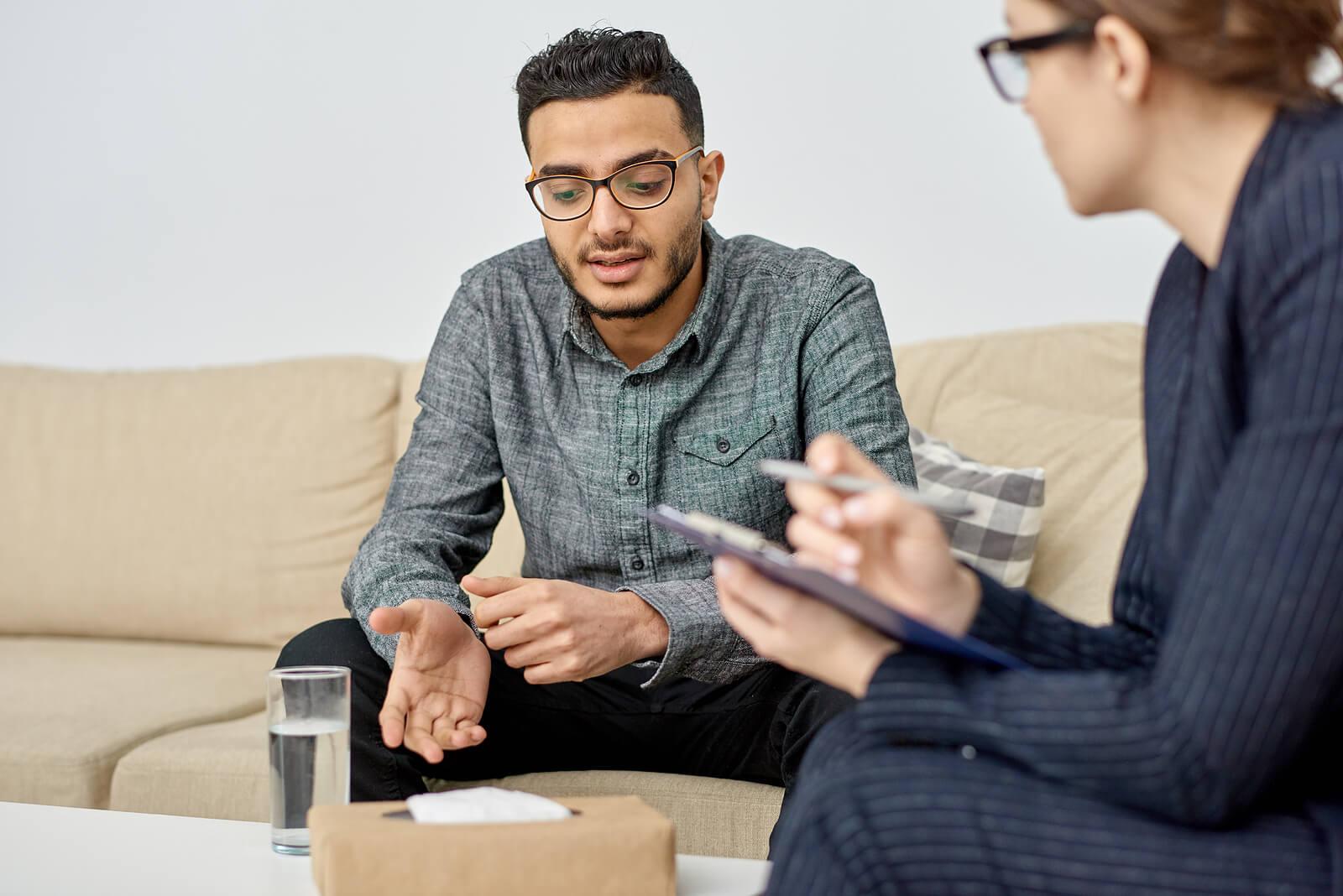 Image of a young man sitting on a couch speaking to a woman holding a clipboard. If you struggle with BPD, discover how and adult intensive outpatient program in Houston, TX can help you manage your symptoms.