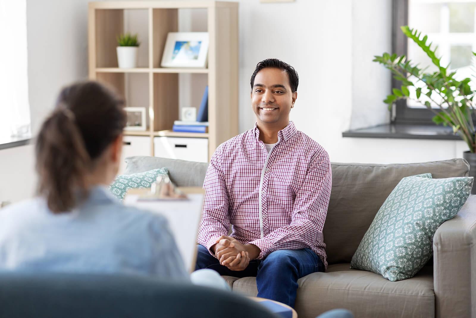 Image of a smiling man sitting on a couch opposite a therapist. If you find yourself stuck unable to move forward due to anxiety, find support with adult IOP in Houston, TX.