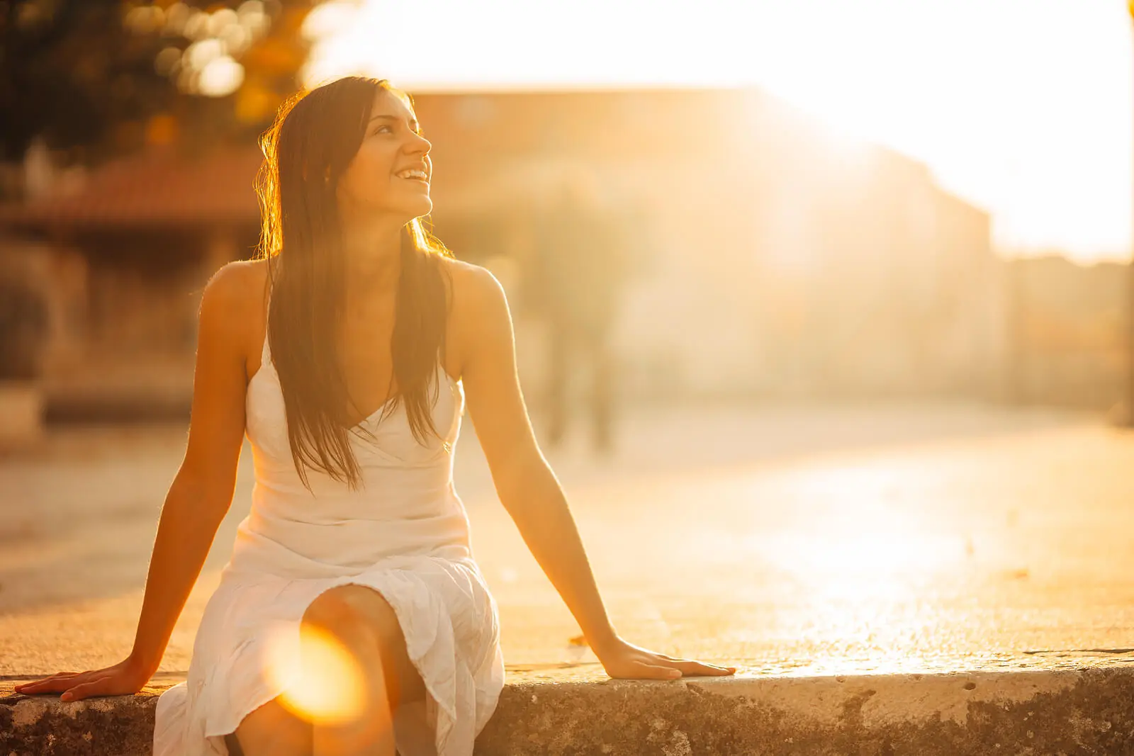 Image of a happy woman sitting on a step looking up at the sky on a sunny day. Begin to build emotional resilience and manage your emotions with mindfulness used in adult IOP in Houston, TX.
