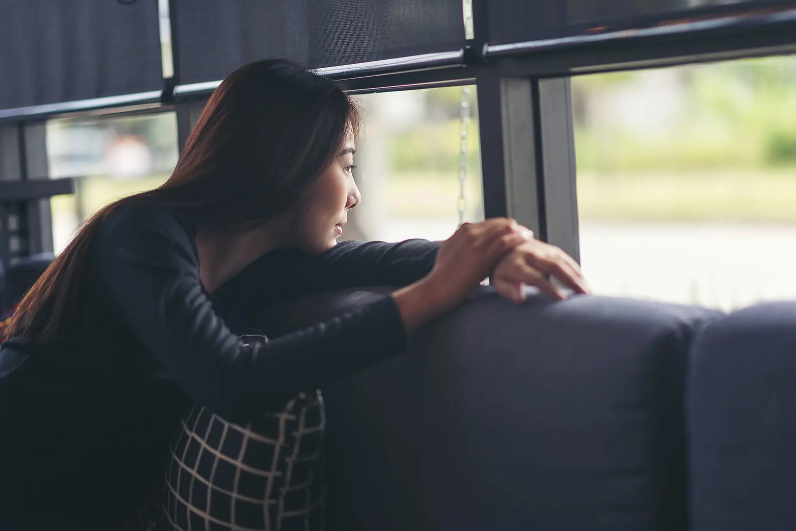 Image of a woman sitting on a couch resting her head on her arm looking out a window in thought. If you're looking to work on your overwhelming emotions find support with an adult IOP in Houston, TX.