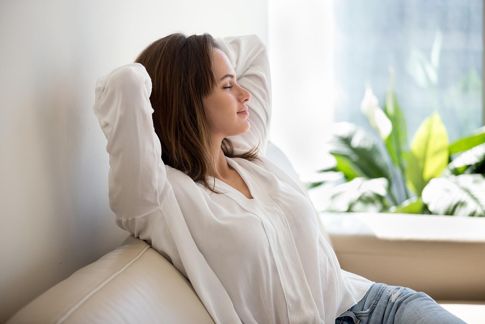 Image of a happy woman sitting on a couch with her hands behind her head relaxing. With an adult IOP in Houston, TX you can begin to manage your BPD with DBT.