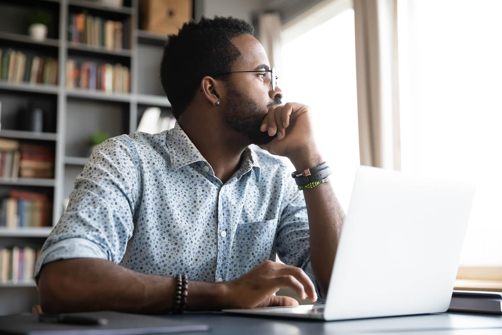 Image of an African American man sitting at a desk with a laptop looking out a window in thought. Discover how mindfulness in an adult IOP in Houston, TX can help you cope with overwhelming emotions.