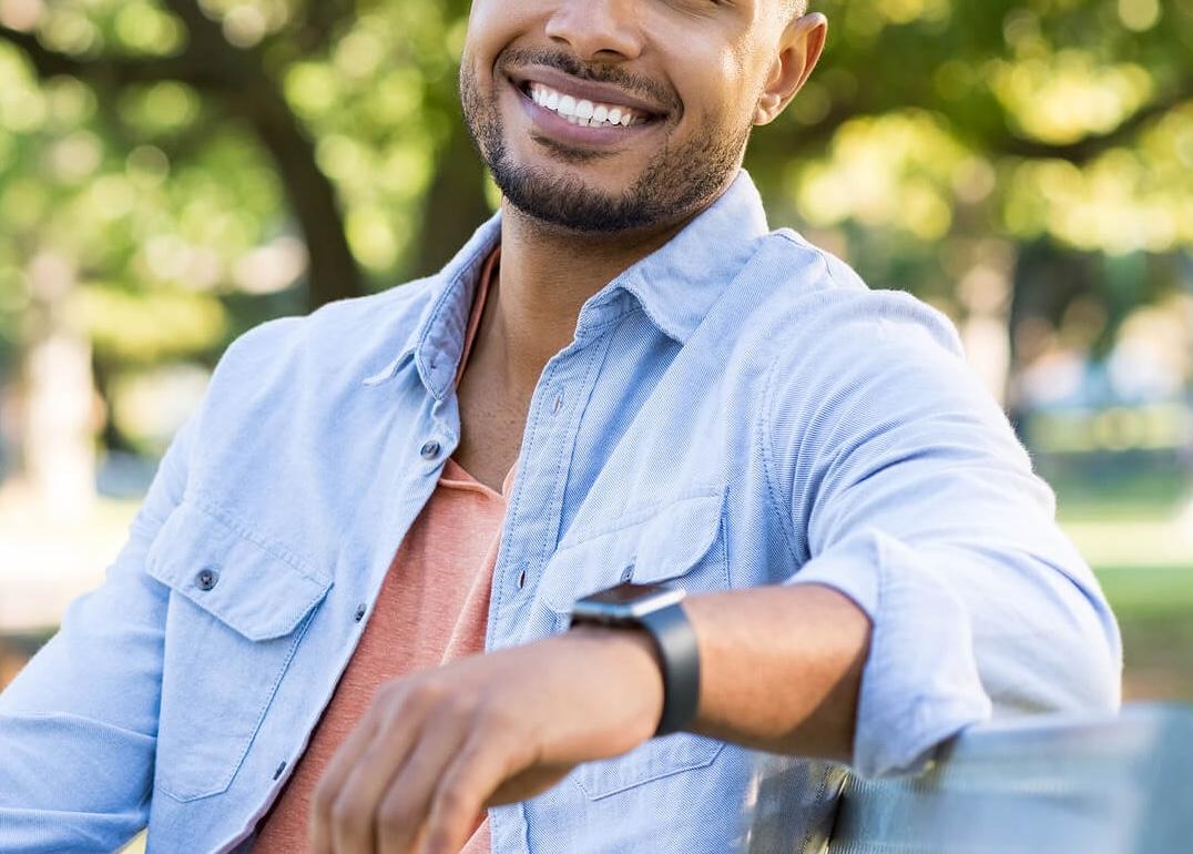 Image of a smiling young African American man sitting on a bench on a sunny day. Begin to control your intense emotions in healthy ways in an Adult IOP in Houston, TX.