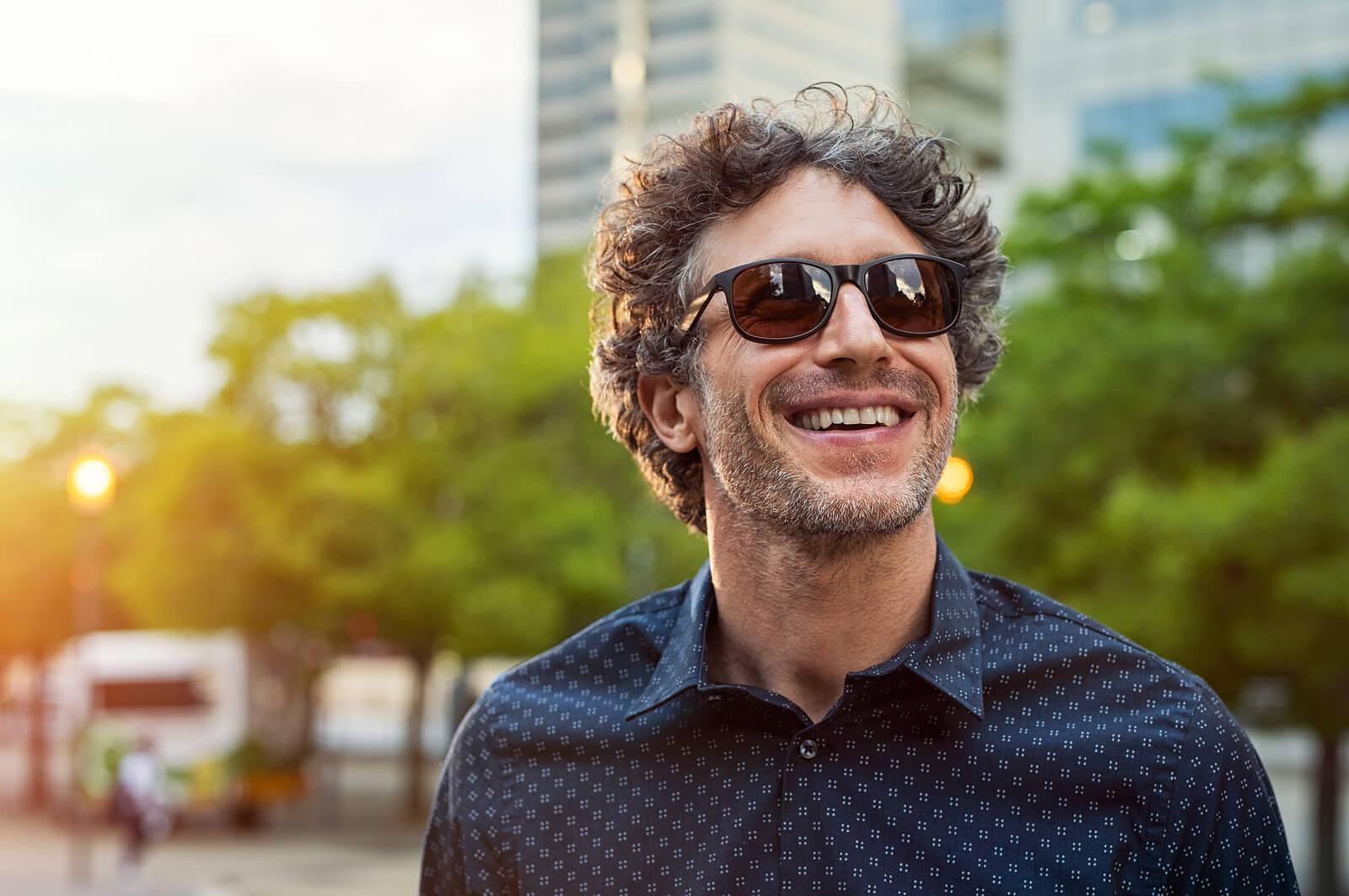 Image of a smiling mature man walking outside with sunglasses on. Begin improving your impulse control and take back your life with the help of DBT used in an Adult IOP in Houston, TX.