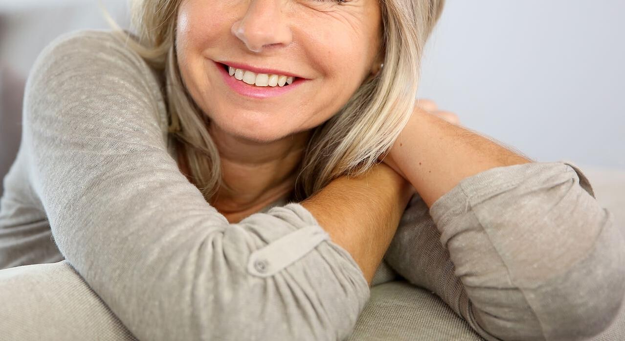 smiling mature woman | adult iop in houston, tx | adult intensive outpatient program in houston, tx | intensive outpatient program houston | iop program houston | 77022 | 77024 | 77057 Smiling mature woman sitting on a couch. Begin healing and overcoming the negative unhealthy patterns keeping you from moving forward with an adult IOP in Houston, TX.