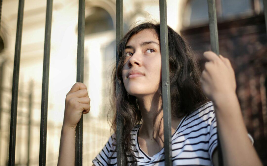 Sad girl teen looking through iron bars