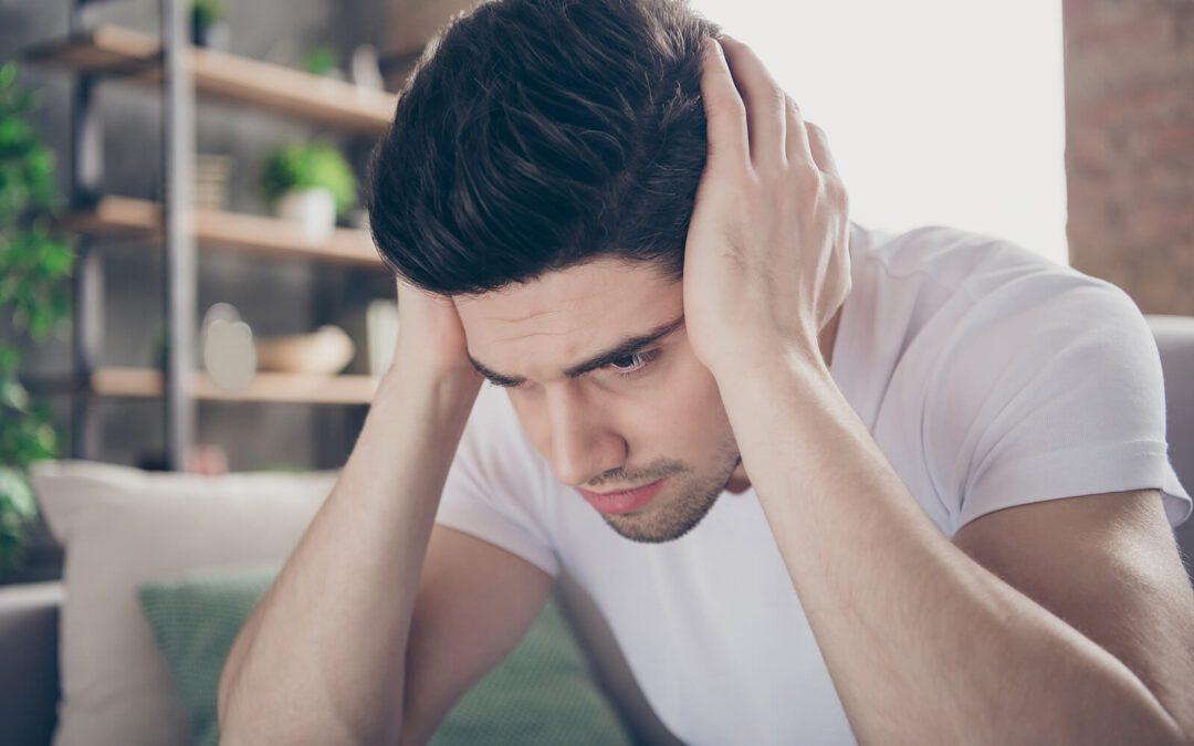 Stressed man sitting on a couch covering his ears. If you're feeling stuck from ADHD perfectionism, find support with perfectionism treatment in Houston, TX.