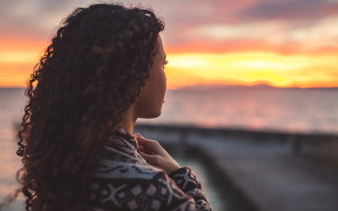 Peaceful woman looking at the ocean as the sun sets. Overcome your perfectionistic thinking and begin healing with the help of perfectionism treatment in Houston, TX.