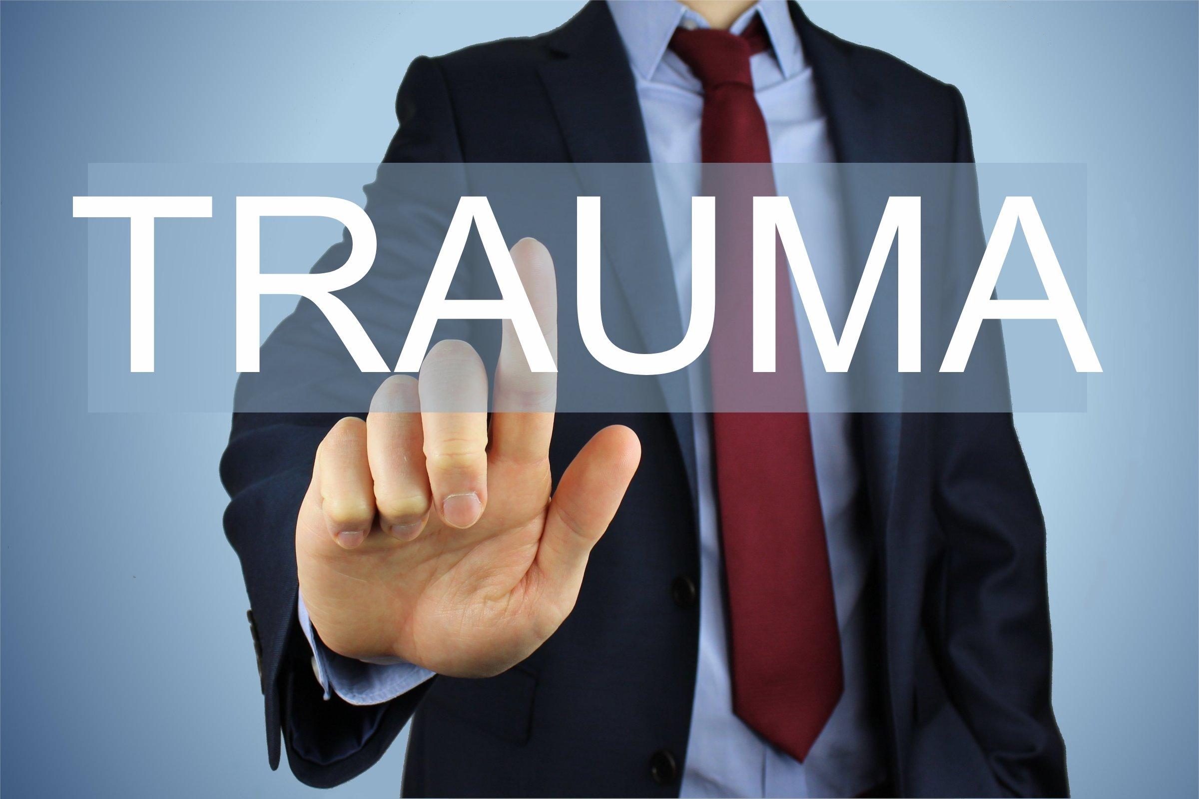 The word "trauma" written in large letters across the chest of a male with a finger to the word